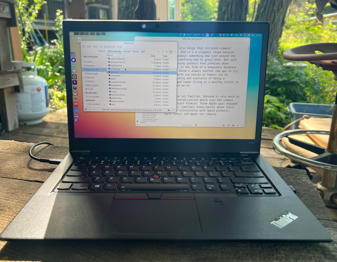 A ThinkPad laptop sitting on a small wooden table. The screen showing a Linux desktop with two app windows visible.